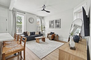 A modern living room with a sofa, coffee table, dining table, chairs, and a ceiling fan.