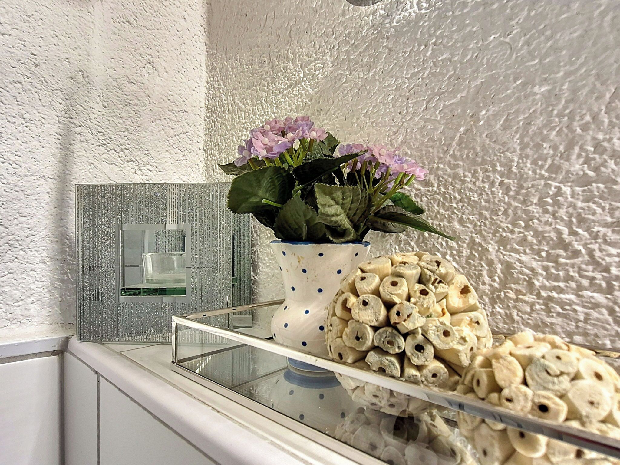 Een badkamer met een witte, gestructureerde wand, een glazen douchecabine, een witte kast en een vaas met bloemen.