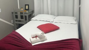 A bedroom with a bed, white curtains, a red pillow, a white towel, and a grey chair. - Pousada e Hostel Flórida  (São Carlos)