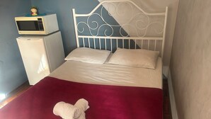 A bed with a white headboard, two pillows, a red blanket, and a rolled towel on the footboard. - Pousada e Hostel Flórida  (São Carlos)