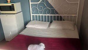 A bed with a white metal headboard, a red blanket, and a white pillow. - Pousada e Hostel Flórida  (São Carlos)