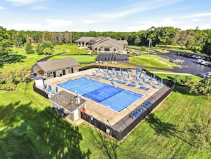 Piscina com espreguiçadeiras e guarda-sóis, cercada por uma área vedada e um edifício.