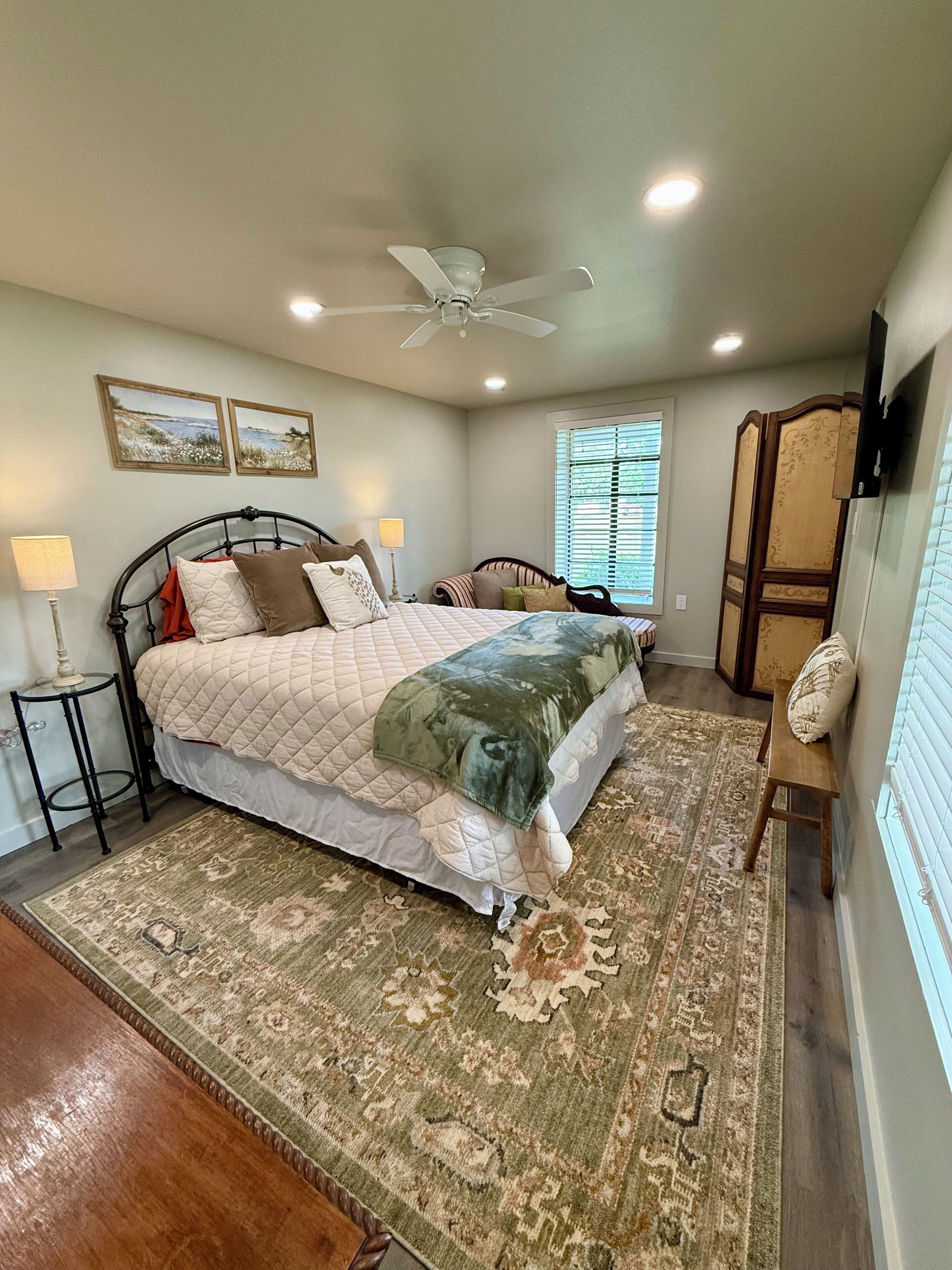 A bedroom with a bed, a ceiling fan, a window, a nightstand, a lamp, and a decorative screen.