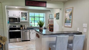 Une cuisine avec des meubles blancs, un four à micro-ondes, un four et un évier. Au-dessus de l’évier, on peut lire une inscription : « BON APPÉTIT ».