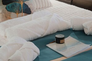 Ein ordentlich gemachteres Bett mit weißen Leinen, eine kleine Schale und eine gedruckte Karte auf einer türkisfarbenen Oberfläche.