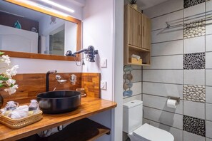 Ein Badezimmer mit einem Holzbadezimmerhocker, einem schwarzen Waschbecken, einem Spiegel und einer Duschkabine mit einem Holzkorpus.