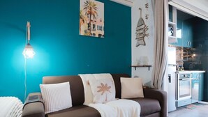 En stue med en brun sofa, en lampe, et billede og et køkken, der kan ses gennem en åben dør.