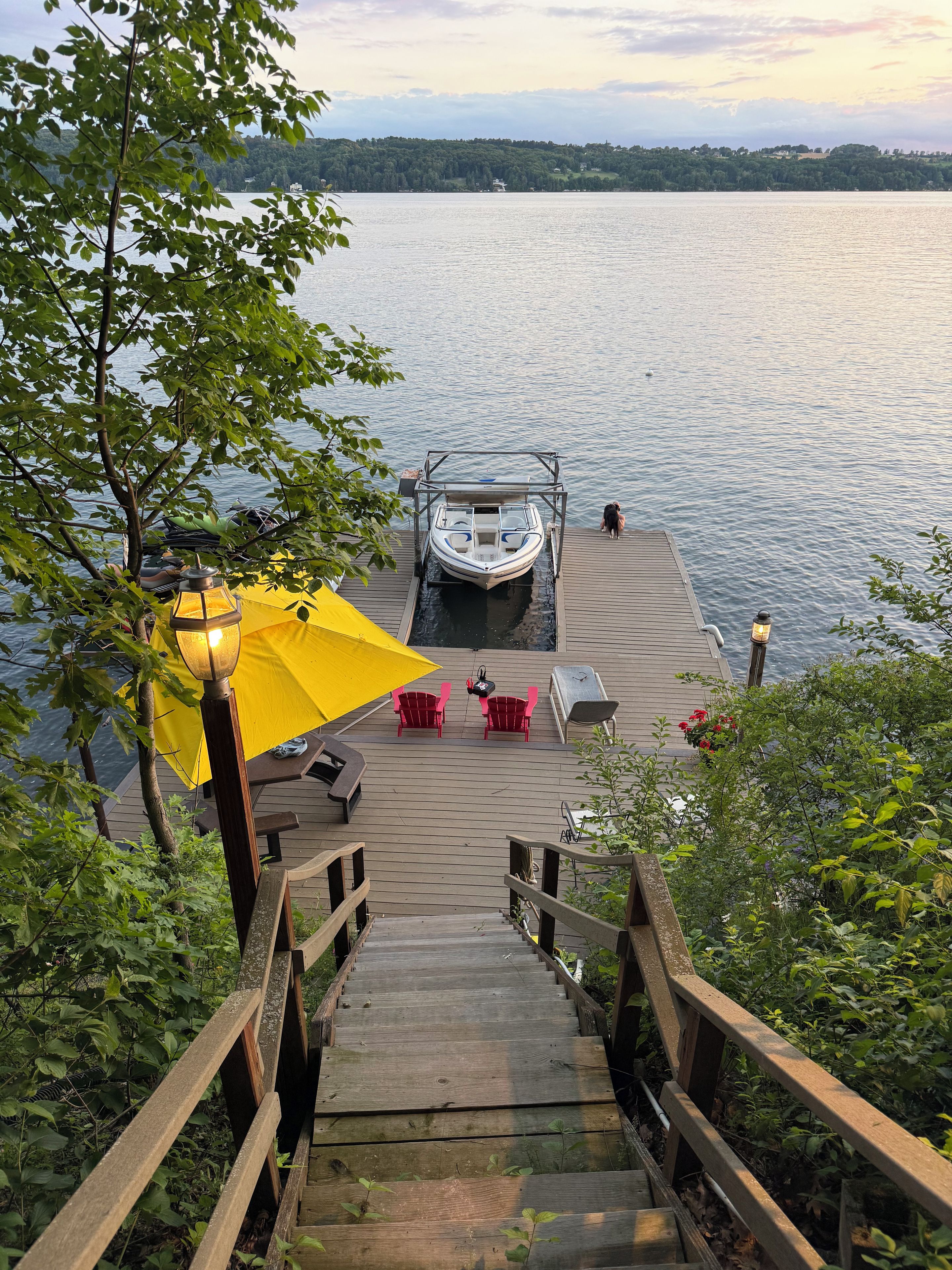 A wooden dock leading to a boat, with a yellow umbrella and red chairs on the dock.