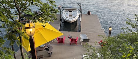 A wooden dock leading to a boat, with a yellow umbrella and red chairs on the dock.