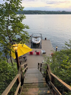 A wooden dock leading to a boat, with a yellow umbrella and red chairs on the dock. - Peaceful secluded roomy lake house, beautiful location lovely waterfrontage (Skaneateles)