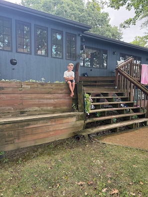 A wooden deck with steps leading to a house with large windows. - Peaceful secluded roomy lake house, beautiful location lovely waterfrontage (Skaneateles)