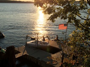 A dock with a boat, a flag, and a person sitting. - Peaceful secluded roomy lake house, beautiful location lovely waterfrontage (Skaneateles)