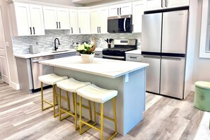 A modern kitchen with white cabinets, stainless steel appliances, a central island with stools, and a tiled backsplash. - Modern Beach House,  Rooftop Deck & Ocean Views, Walk to Beach & Boardwalk (Seaside Heights)