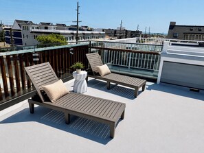 Terraço no telhado com duas espreguiçadeiras, uma mesa pequena com uma planta e guarda-corpo de vidro.