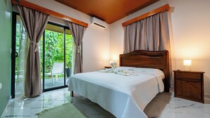 A bedroom with a bed, a nightstand, a lamp, and a view of greenery outside. - River Collection - Villa Tranquil #3 sounds of the river (La Fortuna)