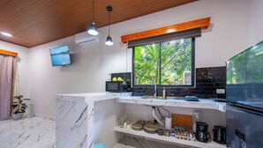 A modern kitchen with a marble countertop, a built-in oven, a window with a view of greenery, and a TV mounted on the wall. - River Collection - Villa Tranquil #3 sounds of the river (La Fortuna)
