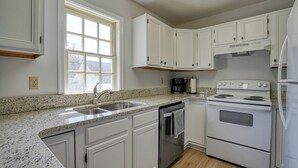 A kitchen with white cabinets, a granite countertop, a stainless steel sink, a coffee maker, and a stove.