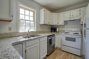 A kitchen with white cabinets, a granite countertop, a stainless steel sink, a coffee maker, and a stove.