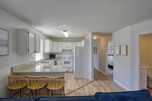 A modern kitchen with white cabinets, a granite countertop, and a built-in oven. There are wooden bar stools and a blue rug.
