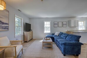 A living room with a blue sofa, a wooden coffee table, a TV, and a large window.