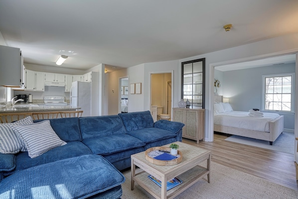 A modern living room with a blue sofa, a coffee table, and a kitchen in the background.