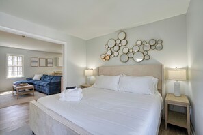 A bedroom with a large bed, a sofa, two bedside tables with lamps, a wall art piece, and a door leading to another room.