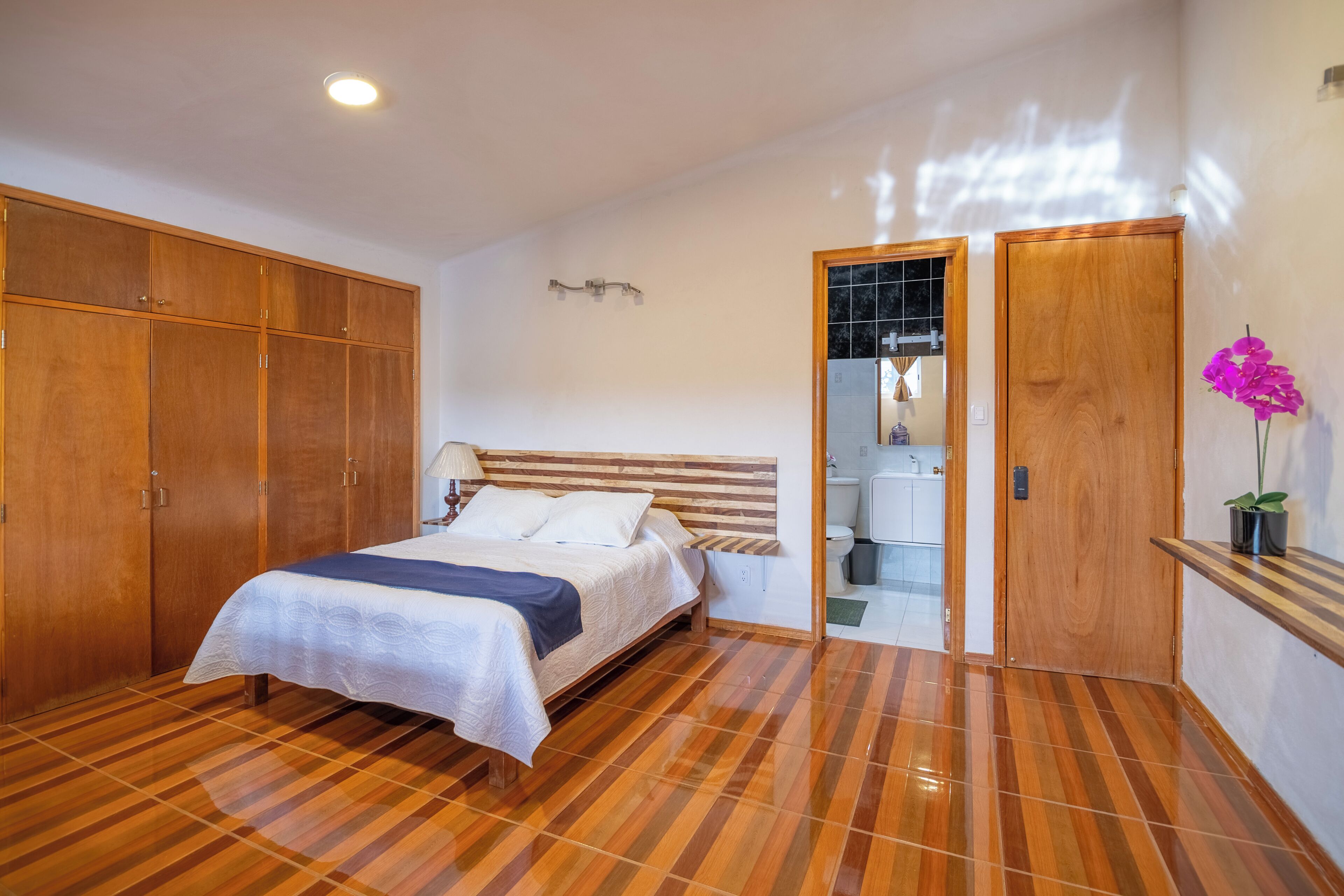 A bedroom with a bed, wooden wardrobe, and a bathroom visible through an open door.