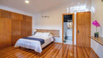 A bedroom with a bed, wooden wardrobe, and a bathroom visible through an open door.