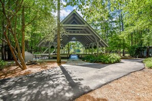 Ein überdachter Pavillon mit einem dreieckigen Dach, umgeben von Bäumen und einem Pflasterweg, der zu ihm führt.