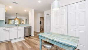 Una cocina moderna con gabinetes blancos, lavavajillas de acero inoxidable y una mesa azul con taburetes.
