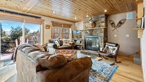 Un salón acogedor con chimenea de piedra, muebles de cuero y un balcón con vistas.