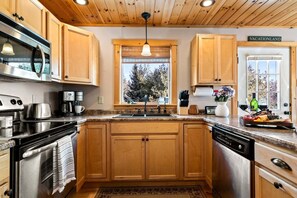 A kitchen with wooden cabinets, stainless steel appliances, a window with a view, and a sign reading 'VACATIONLAND'. - Moose Lodge: 4BR retreat with hot tub, fireplace, and game room. (Bethel)
