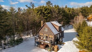 Una cabaña de troncos con porche y terraza, rodeada de bosque y nieve.