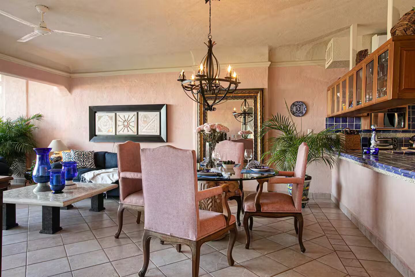 Een eetruimte met een kroonluchter, een tafel, stoelen en een keuken met kasten.