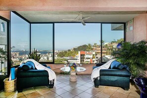 A balcony with two sofas, a table with a decorative bowl, and a view of a cityscape. - 2-bedroom Hacienda Condo in Puerto Vallarta Spectacular View-Pool-Walk to Beach (Puerto Vallarta)