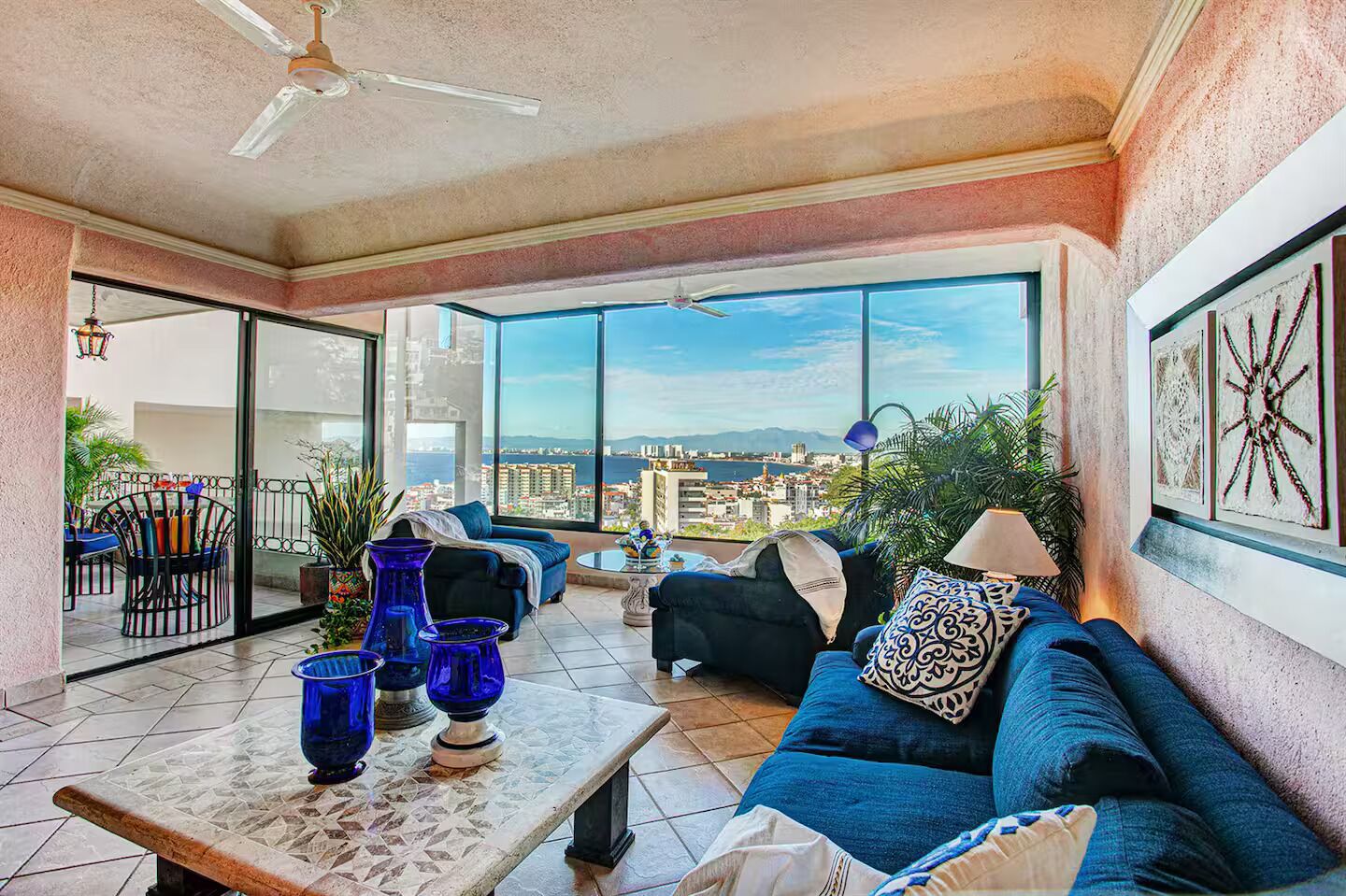Ein geräumiger Balkon mit Blick auf die Stadt, eine Couch mit Zierkissen und blaue Vasen auf einem Tisch.