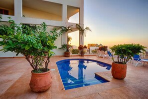 A pool area with potted plants, lounge chairs, and a building in the background. - 2-bedroom Hacienda Condo in Puerto Vallarta Spectacular View-Pool-Walk to Beach (Puerto Vallarta)