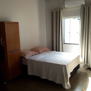 Ein Schlafzimmer mit Bett, Kleiderschrank, einem Fenster mit Vorhängen und einer Klimaanlage.