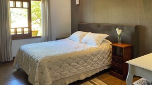 A bedroom with a bed, a nightstand, a vase with flowers, a window with curtains, and a wall-mounted light. - Beautiful and comfortable house with security in a gated community near São Paulo. (Atibaia)