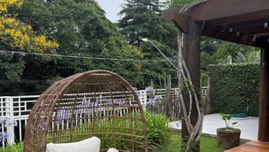 A wicker chair with cushions in a garden area with a wooden deck and a pergola. - Beautiful and comfortable house with security in a gated community near São Paulo. (Atibaia)
