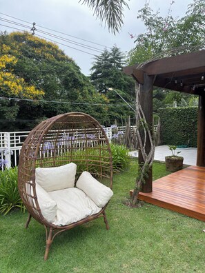 A wicker chair with cushions in a garden area with a wooden deck and a pergola.