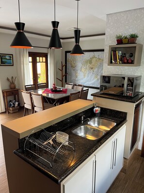 A modern kitchen with a central island, black pendant lights, a stainless steel sink, and a world map on the wall.