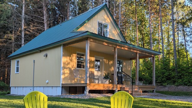 A house with a porch, two chairs, and a grill. - Cosy on-farm Cottage near Hardwood Lake. Fire pit, hiking trails, Beach nearby (Palmer Rapids)
