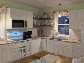 Una cocina con armarios blancos, microondas, estufa, pileta y ventana con vistas.
