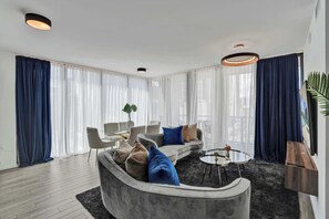 Ein modernes Wohnzimmer mit einer gebogenen, grauen Couch, einem Couchtisch und einem Essbereich mit Stühlen.