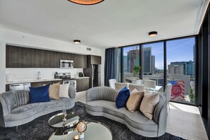 A modern living room with a grey sofa, a coffee table, and a view of the city through large windows. - X Lounge IX Signature | 3 BR/3 Ensuite Residence (Miami)