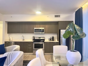 A modern kitchen with stainless steel appliances, a dining table with chairs, and a large potted plant. - X Lounge IX-Signature Skyline Residence (Miami)