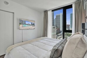 Ein Hotelzimmer mit Bett, Wandfernseher und großem Fenster mit Vorhängen.