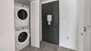 Uma lavanderia com duas máquinas de lavar de abertura frontal e uma porta com aviso de 'Proibido Fumar'.