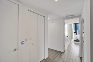 Ein Flur mit weißen Türen, einem sichtbaren Rauchmelder und Blick auf eine Stadtlandschaft durch ein Fenster.